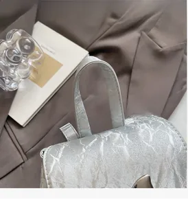 Silver commuter backpack with metallic pleated texture and butterfly buckle on a blazer