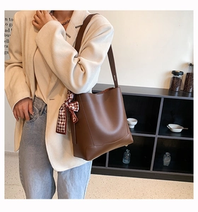 Brown leather bucket bag with silk scarf detail worn by a model in a beige suit