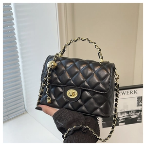 Détail d'un sac en cuir noir matelassé avec chaîne dorée et boule décorative en métal