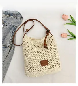 Detail of hollow woven beige tote with leather brand tag and adjustable brown strap