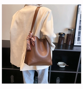 Brown leather bucket bag with plaid scarf detail worn over a light blazer