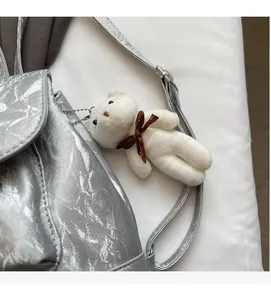 Close-up of silver crinkled backpack with a cute white teddy bear plush charm and ribbon