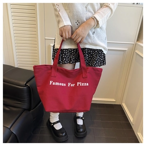Dettaglio borsa tote in tela rossa con stampa Famous For Pizza tenuta da una persona
