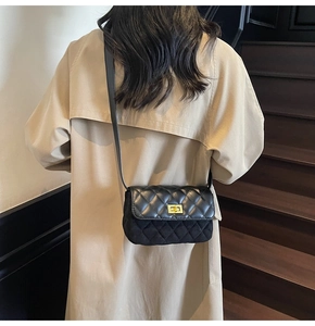 Close-up of black quilted crossbody bag with gold metal buckle worn with beige coat