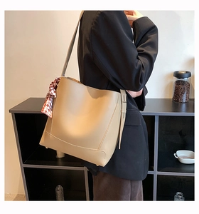 Detail of beige faux leather tote bag with red checkered scarf on model shoulder