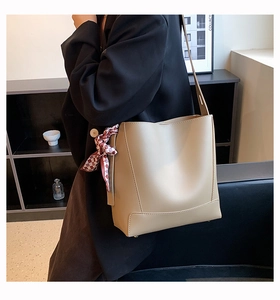Detail of a beige bucket bag with a red plaid scarf tied on the strap for office commute