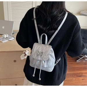 Detail view of silver butterfly backpack featuring a cute teddy bear charm on model back
