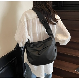Model wearing large black nylon hobo bag on shoulder against minimalist wooden stairs