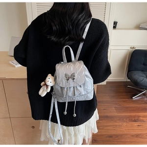 Silver wrinkled leather backpack detail featuring metal butterfly buckle and teddy bear charm