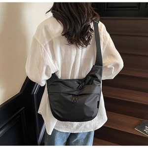 Detail shot of a black large nylon crossbody bag worn by a model on wooden stairs