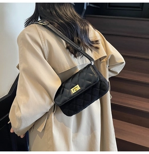 Detail of a black quilted shoulder bag with gold metal lock on a model's shoulder
