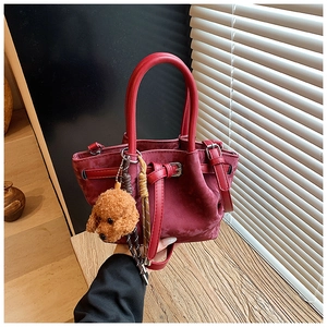 Détail du sac à main en daim bordeaux avec sangle en cuir et breloque chien
