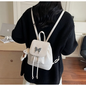 Detailed view of white PU leather backpack with silver butterfly buckle and plush bear charm