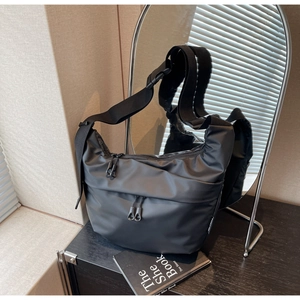 Close-up of black nylon crossbody bag with dual zip pockets on dark wood table