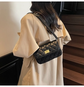 Close-up of black quilted shoulder bag with gold metal clasp on a model's beige coat