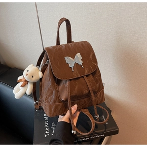 Detail of dark brown backpack with silver butterfly buckle and white bear plush charm