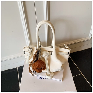 Détail d'un sac à main plissé blanc crème avec un joli pendentif chien en peluche marron