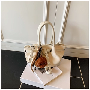 Gros plan du sac seau à cordon crème avec un pendentif chiot en peluche marron sur un livre