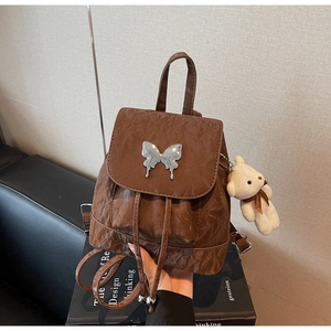Detail of vintage brown backpack with metallic butterfly clasp and plush bear charm
