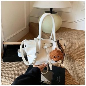 Détail du sac seau en cuir blanc avec un charmant ours en peluche sur un tapis tissé