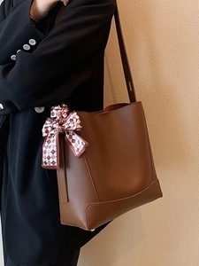 Deep brown leather tote bag with checkerboard silk scarf on a model in a black suit