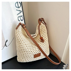 Close-up of cream woven tote bag featuring a leather logo patch and brown shoulder strap