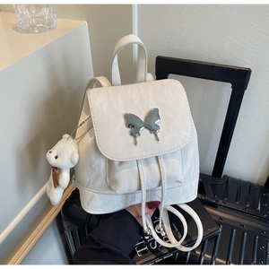 Detail of white textured backpack with silver metal butterfly and plush bear charm