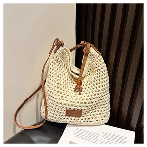 Close-up of beige crochet tote bag featuring brown leather straps and brand logo detail