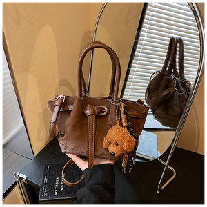 Détail du sac seau marron foncé mat avec boucles métalliques et un charme de chien peluche