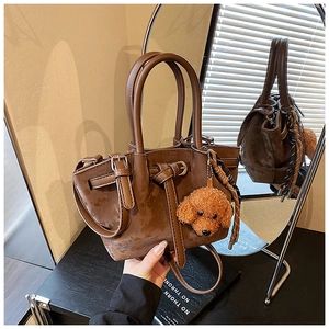 Détail du sac seau en daim marron avec poignée en cuir et breloque ours en peluche