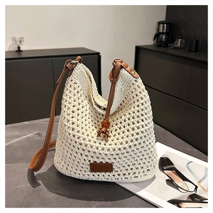 Detail of hollow woven tote bag featuring brown leather strap on marble surface