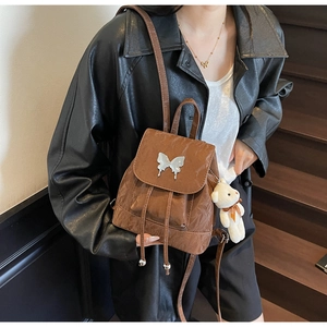 Detailed view of a brown backpack with a silver butterfly buckle and plush bear charm