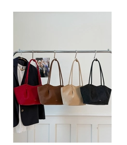 Détail de quatre sacs cabas plissés en rouge, marron, beige et noir suspendus à un rack