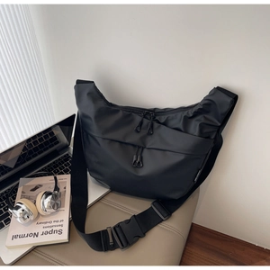Detail of minimalist black nylon crossbody bag featuring a large buckle and wide strap