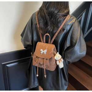 Detail of dark brown backpack with silver butterfly charm and plush bear accessory