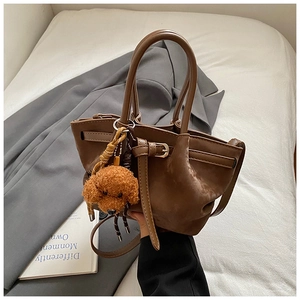 Détail d'un sac à main en cuir marron mat avec breloque chien en peluche et sangle fine