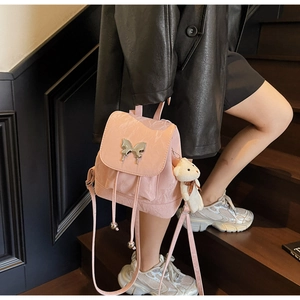 Detail of pink textured backpack featuring a silver butterfly buckle and plush bear charm