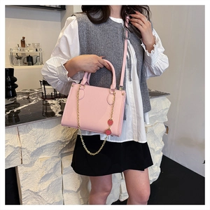 Détail du sac à main en cuir rose avec chaîne dorée amovible et breloques fraises