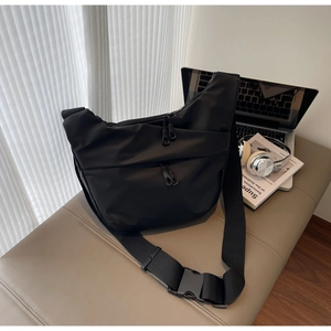 Detail of black nylon sling bag with multiple zipper pockets and wide buckle strap