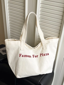 Borsa tote in tela crema con scritte rosse appoggiata su una sedia in pelle nera