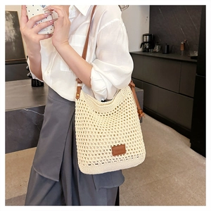 Detailed view of cream hollow woven tote bag with brown leather strap on shoulder
