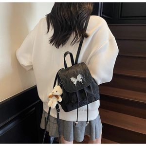 Detail of black pleated backpack featuring silver butterfly hardware and cute bear charm