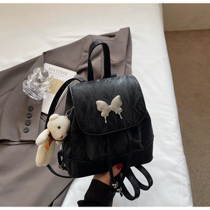 Detail view of black embossed backpack with silver butterfly charm and plush bear pendant