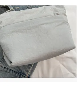 Dettaglio della borsa a secchiello in nylon grigio chiaro con trama morbida e logo su denim