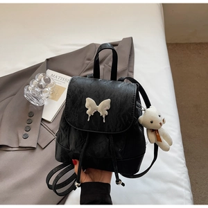 Detail of black pleated PU leather backpack with silver butterfly buckle and plush bear charm