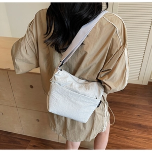 Détail d'un sac seau en nylon crème avec large bandoulière porté par un mannequin