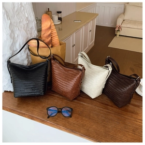 Close-up of woven bucket bags in black, tan, cream, and brown on a wooden surface