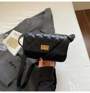 Close-up of black quilted shoulder bag with gold rotating lock and leather strap