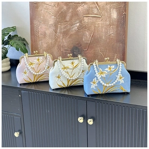 Close-up of three vintage embroidered floral handbags with pearl handles on a wooden table