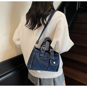 Detail of blue denim crossbody bag with metal buckle and pocket accents on a model